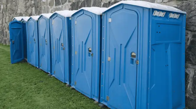 Row of blue portable toilets lined up on grass against a stone wall for event sanitation in Columbia, MO