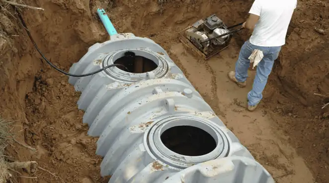 Septic tank installation showing a technician compacting soil around a new poly septic tank in an excavation pit in Columbia, MO